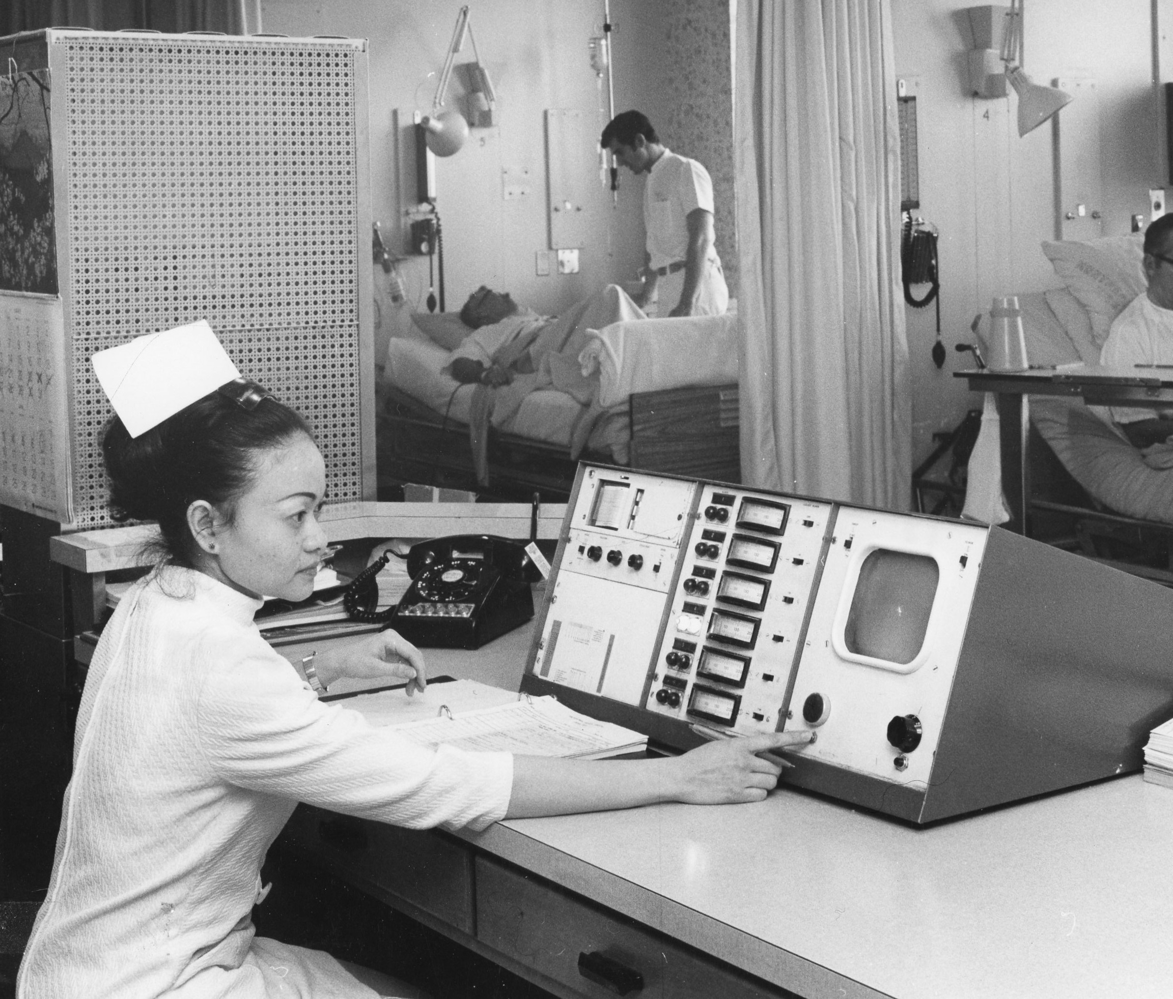 nurse in foreground checks a monitor screen with patients in background