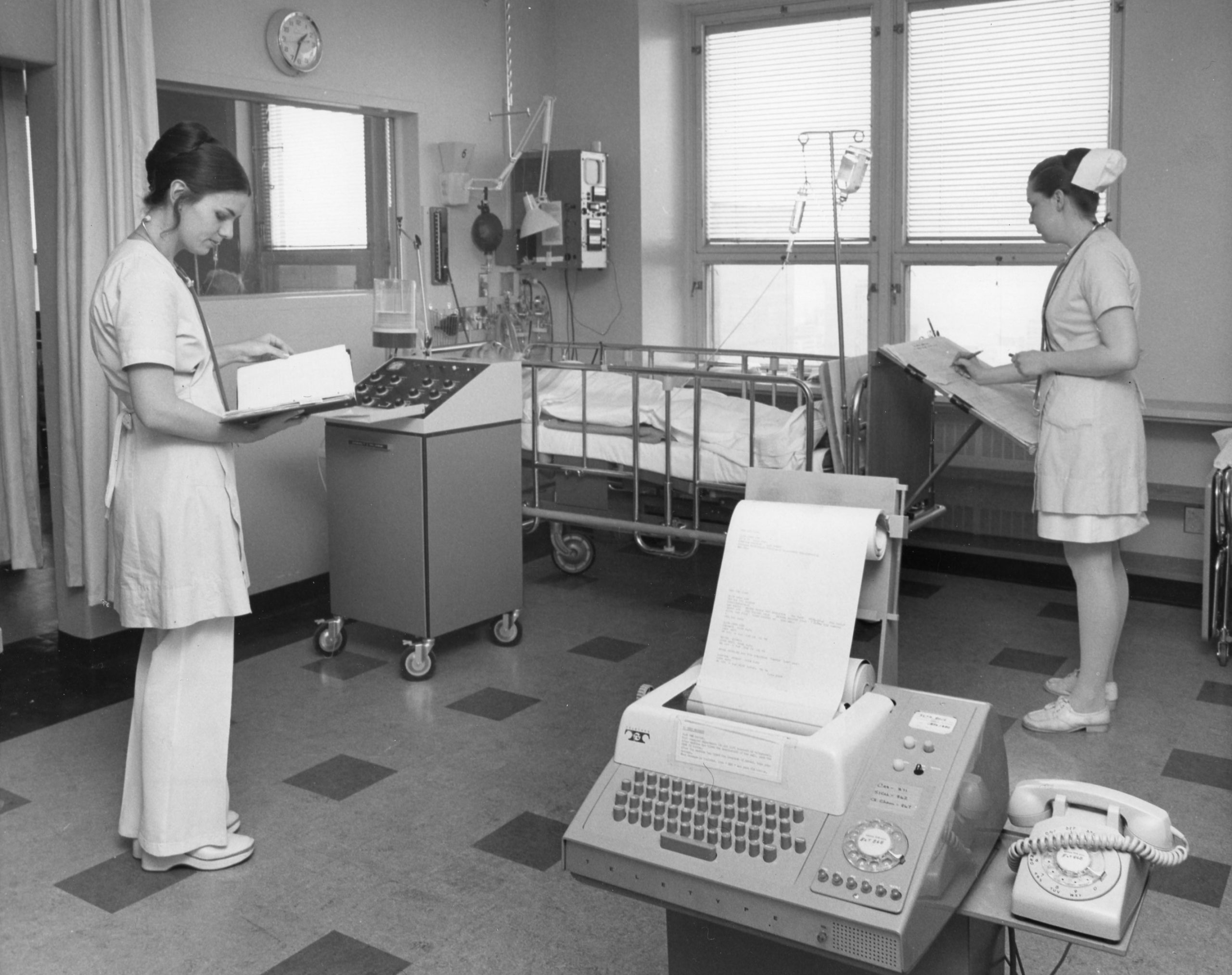 nurses in a medical intensive care unit with machinery in foreground and surrounding bed